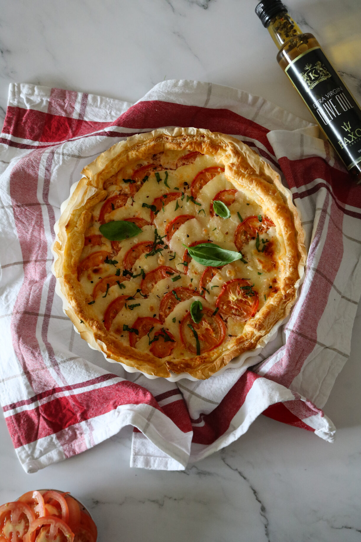 Tarte tomate mozzarella et poulet dorée au four sur une table avec huile d'olive de Paxos