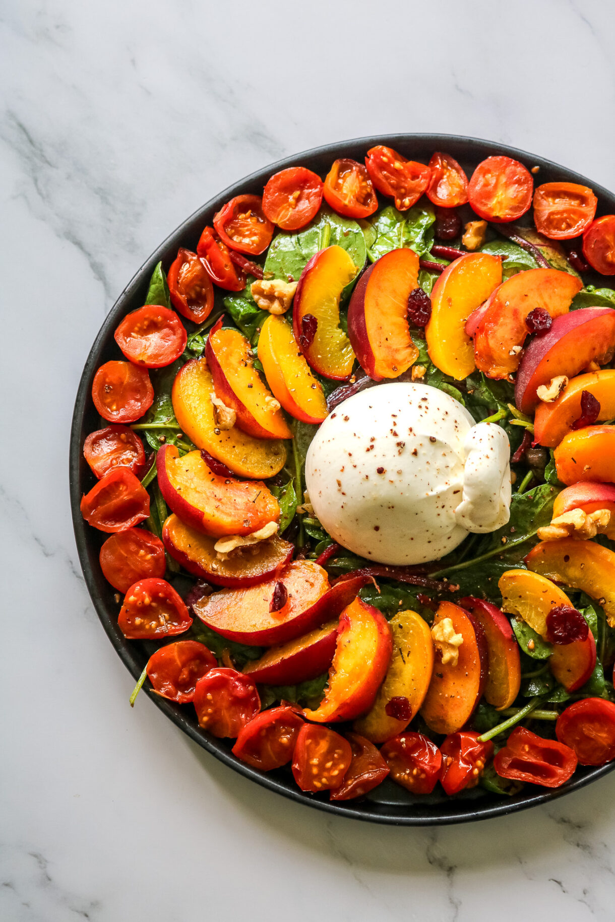 Vue d'ensemble d'une salade avec pêches rôties burrata, pousses épinards et tomates confites