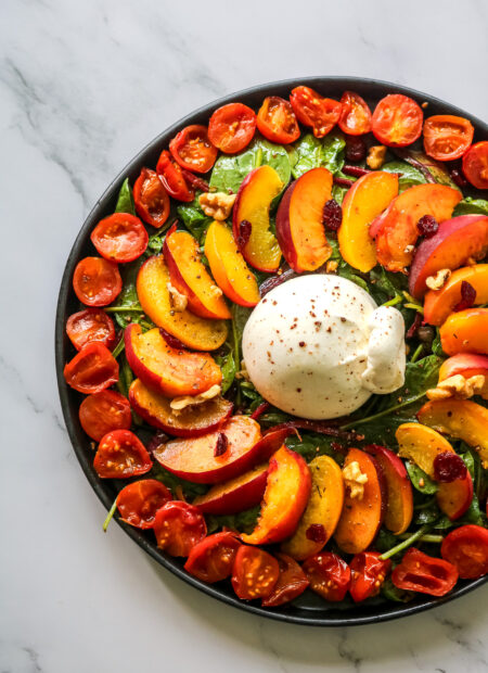 Vue d'ensemble d'une salade avec pêches rôties burrata, pousses épinards et tomates confites