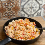 Poêle contenant un risotto méditerranéen contenait avec du riz carnaroli, des morceaux de poulet au citron, des poivrons rouges et jaunes, des carottes et des tomates confites, prêt à être dégusté.