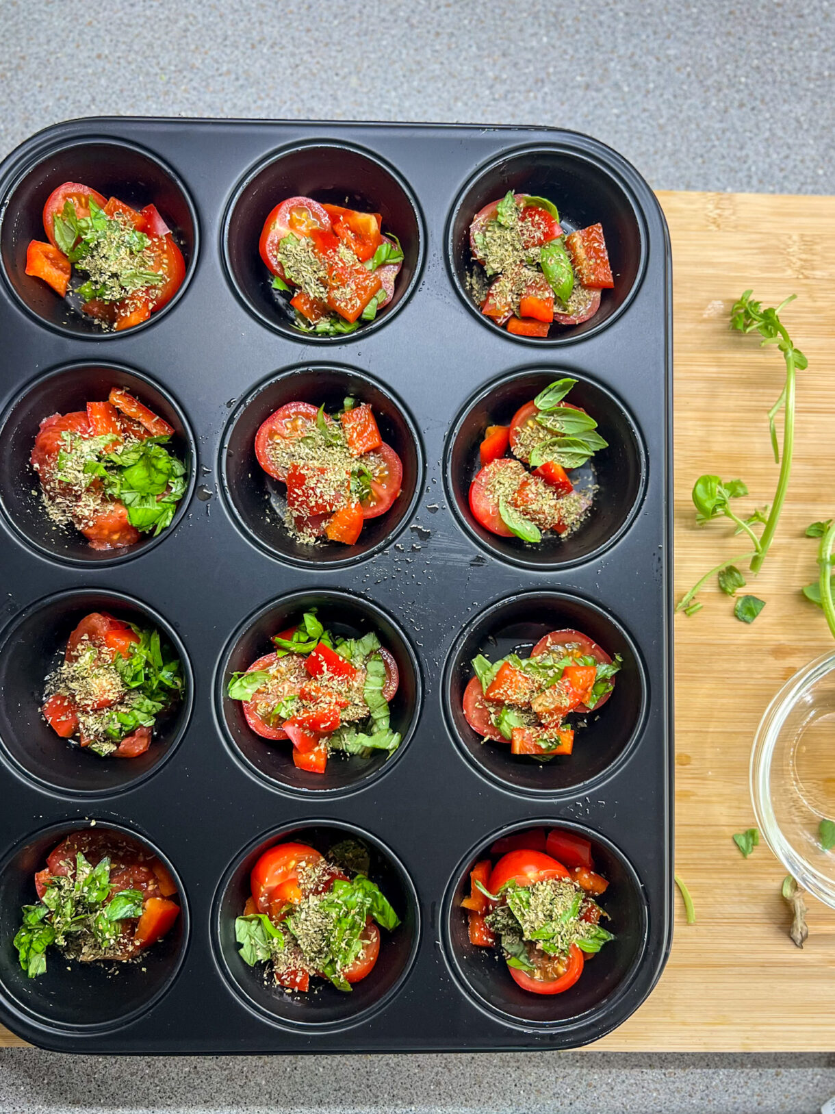 Moule de 12 muffins contenant des tomates cerises, feuilles de basilic, poivrons, et feuilles de basilic