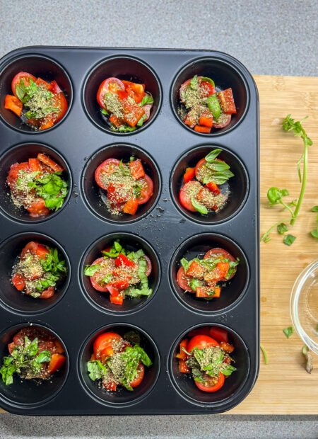 Moule de 12 muffins contenant des tomates cerises, feuilles de basilic, poivrons, et feuilles de basilic