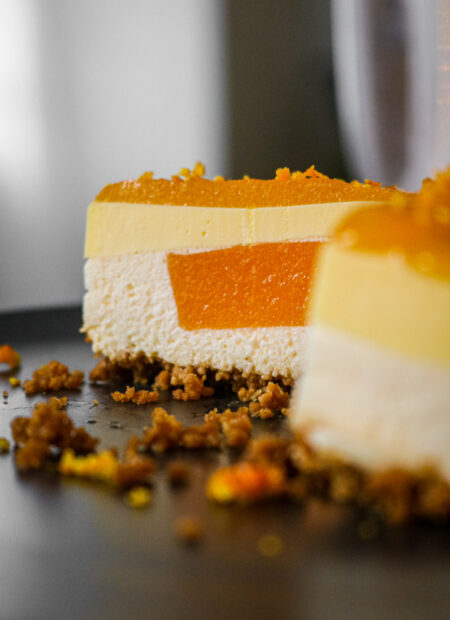 Gros plan d’un entremet à la clémentine avec son glaçage brillant, zestes de clémentine pour finition.