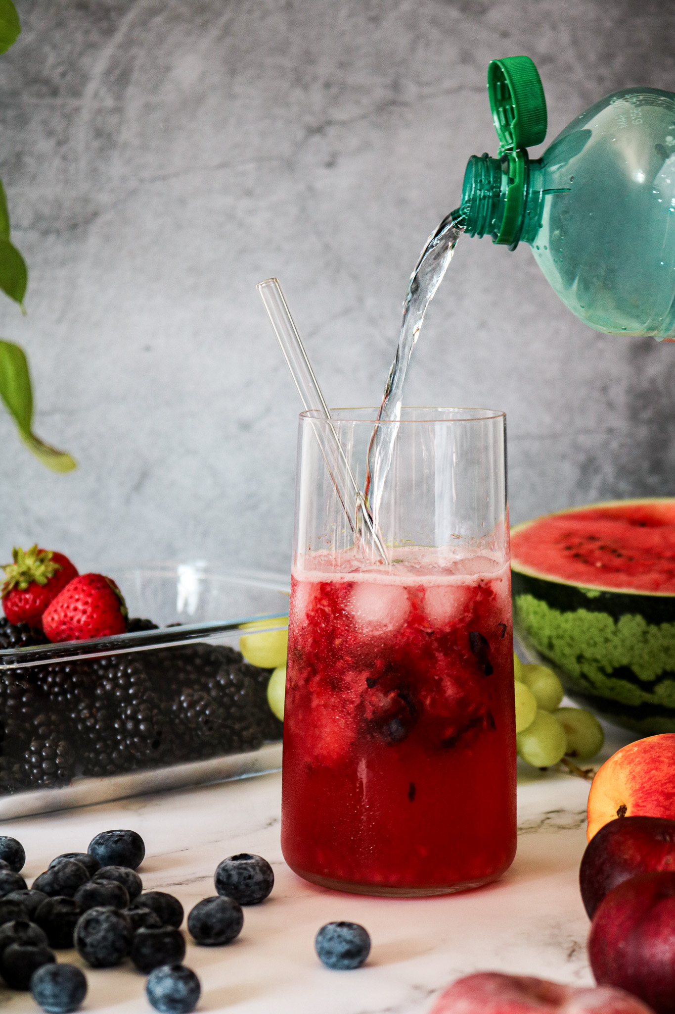 Verser de l'eau gazeuse dans un verre de citronnade maison aux fruits rouges et glaçons
