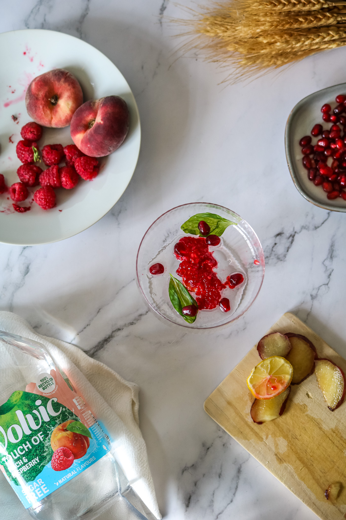 Mocktail peche framboise à la Volvic sur une table en marbre entouré de fruits d'été