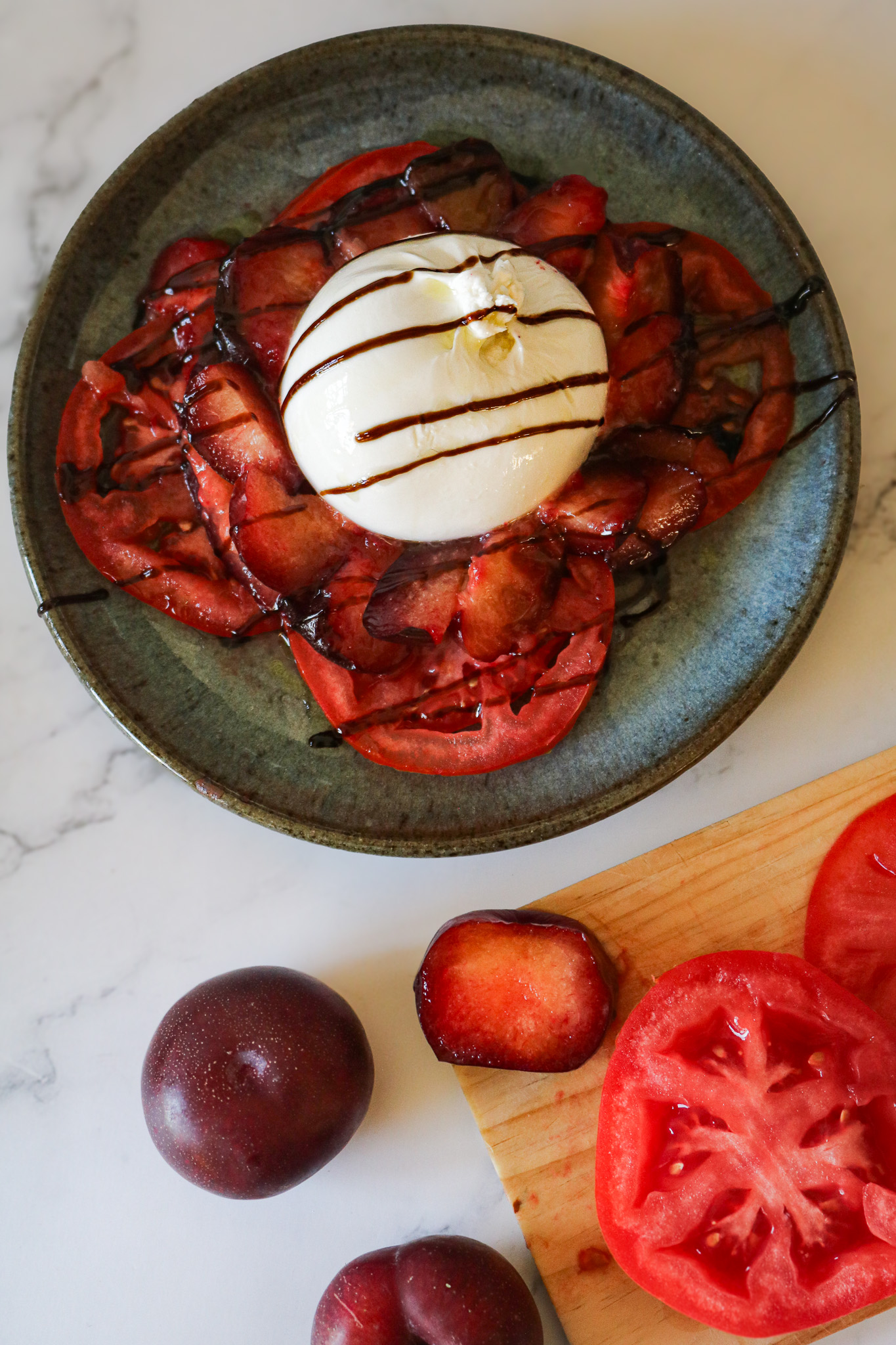 Salade fraicheur tomate prune burrata dresse dans une assiette avec une vinaigrette foncée