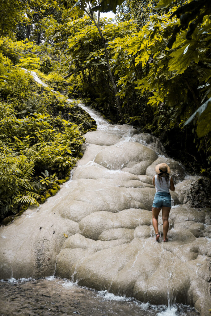 Adeline Bernard debout sur les rochers clairs de la Sticky Waterfall à Chiang Mai, entourée de végétation luxuriante